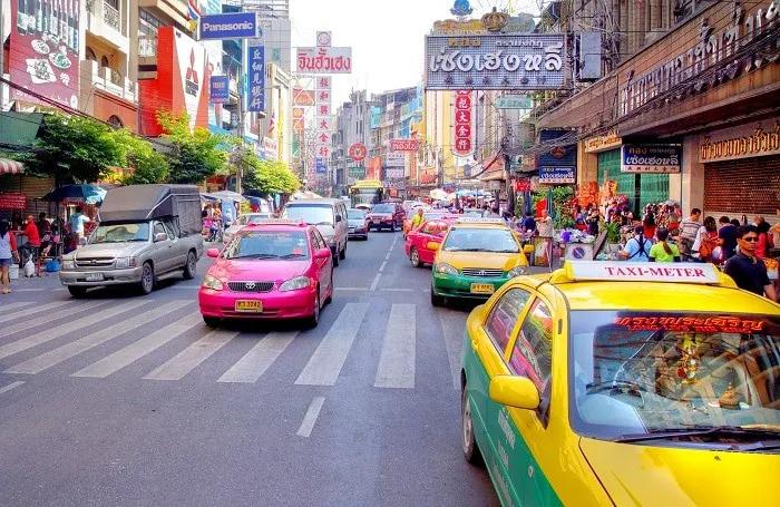 Tráfico en una calle de Bangkok con taxis coloridos y tiendas.
