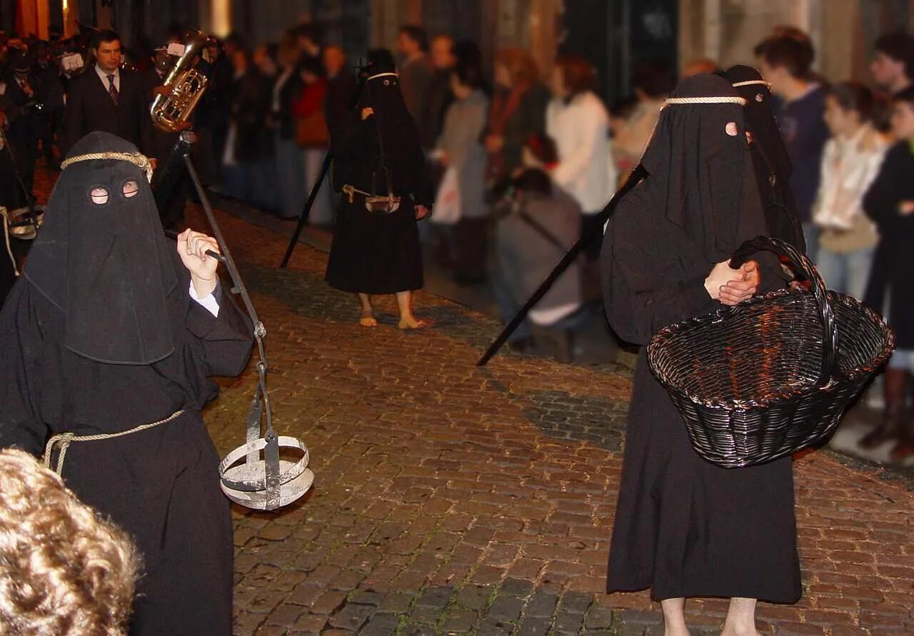 Participantes da Semana Santa vestidos com túnicas pretas, em uma procissão noturna.