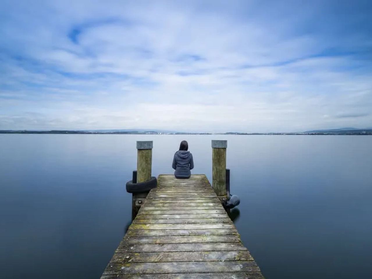 mulher sentada num cais de madeira na margem de um lago