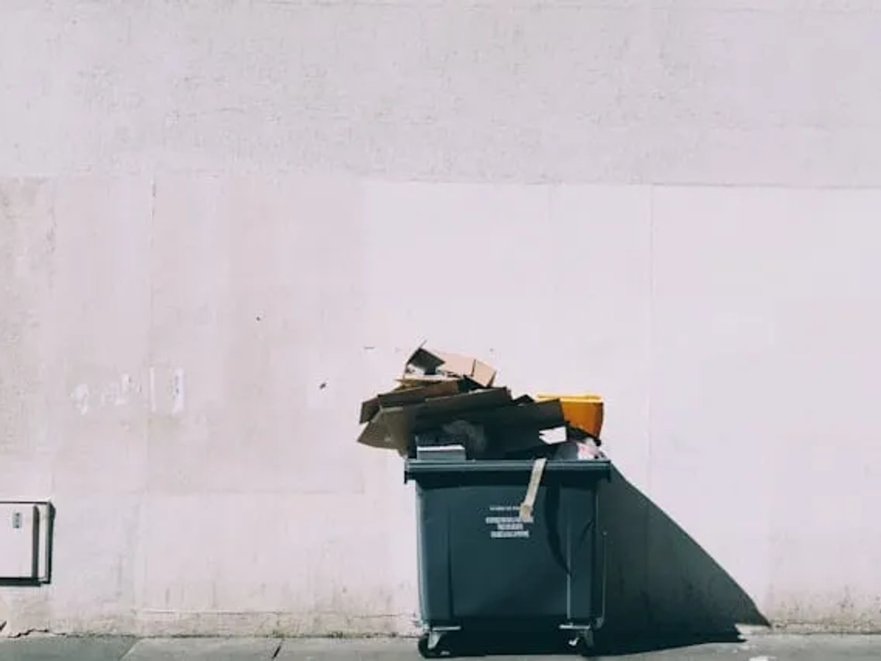 caixote do lixo encostado a uma parede branca