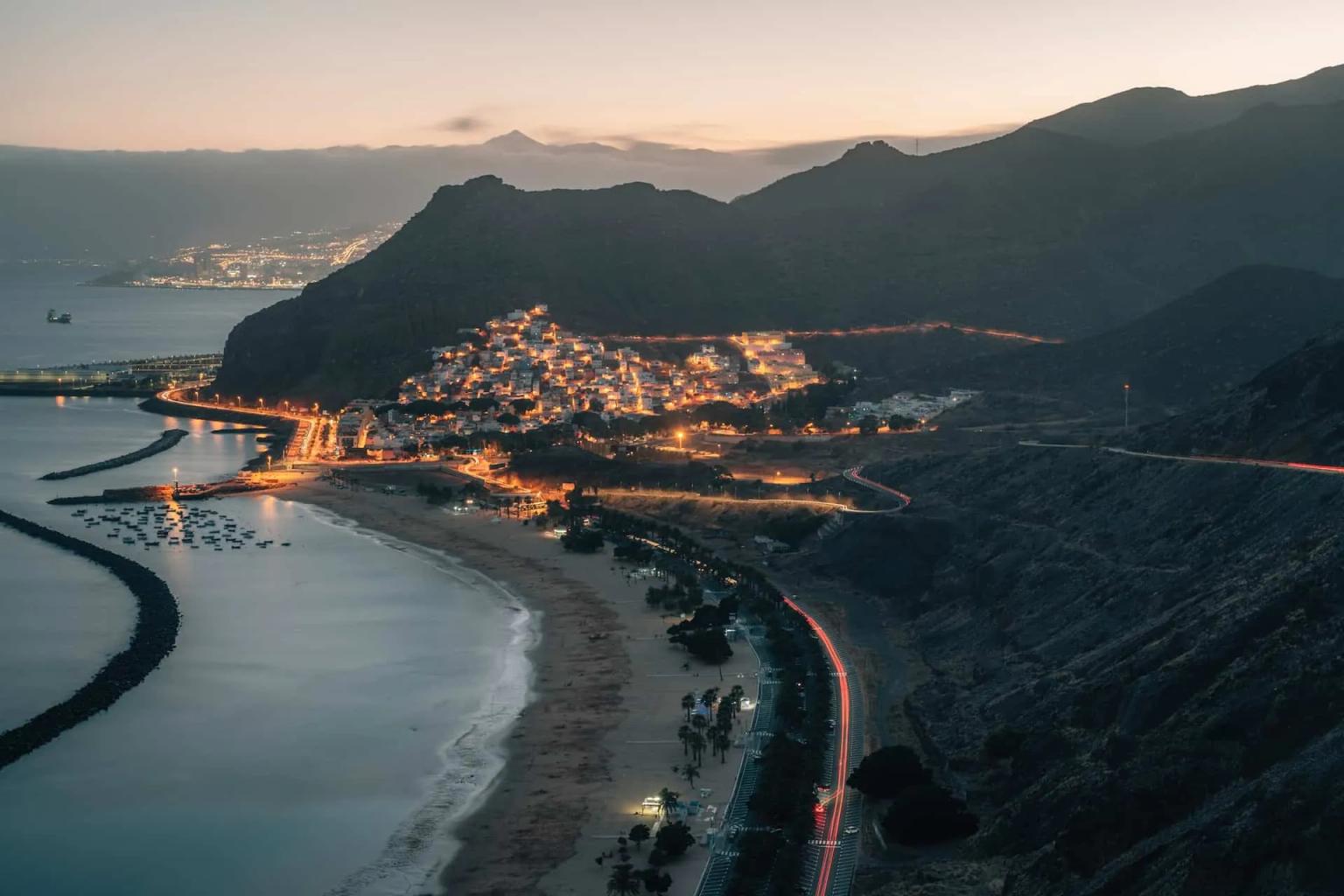 Vista noturna de uma costa em Tenerife, com montanhas e luzes da cidade.