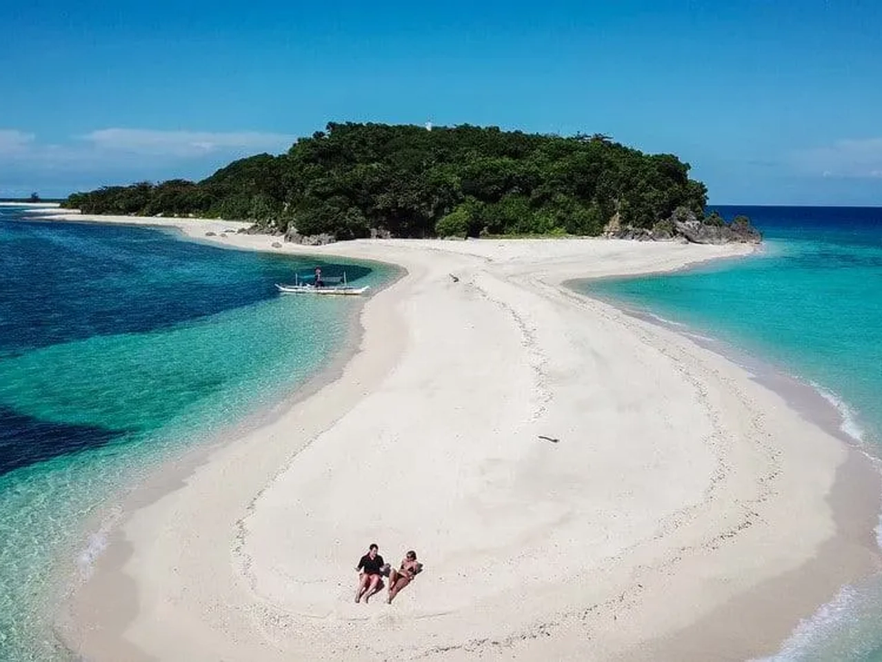 Playa paradisíaca con arena blanca y agua turquesa, rodeada de vegetación.