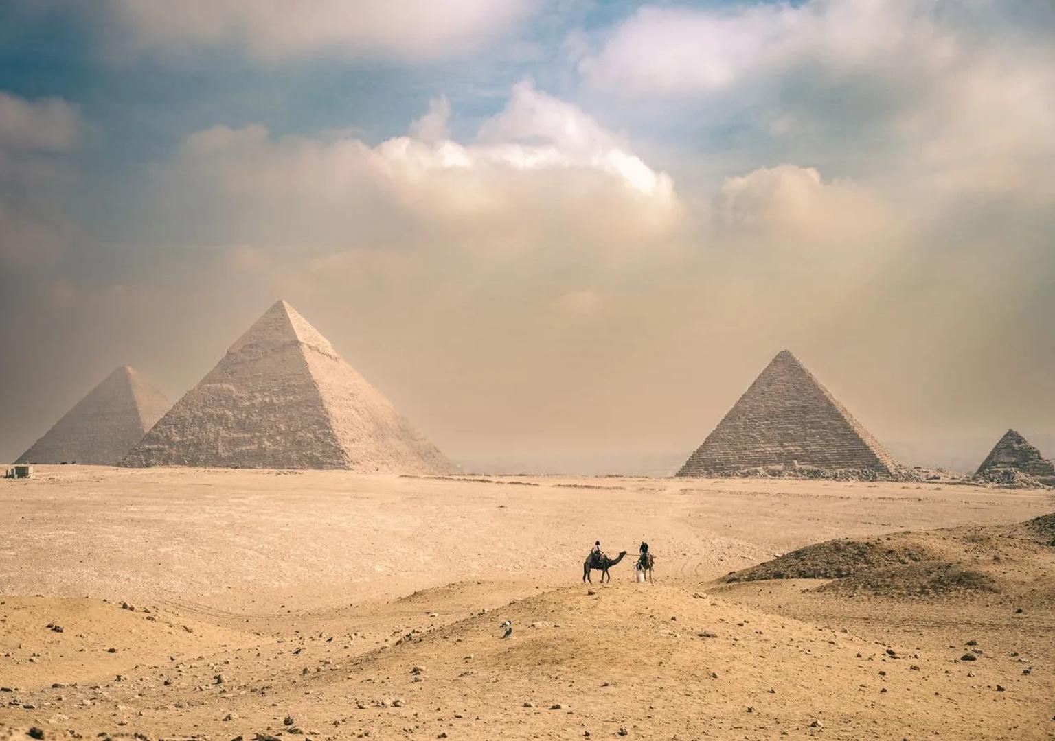Piramidi di Giza sotto un cielo soleggiato, con viaggiatori in lontananza sui cammelli