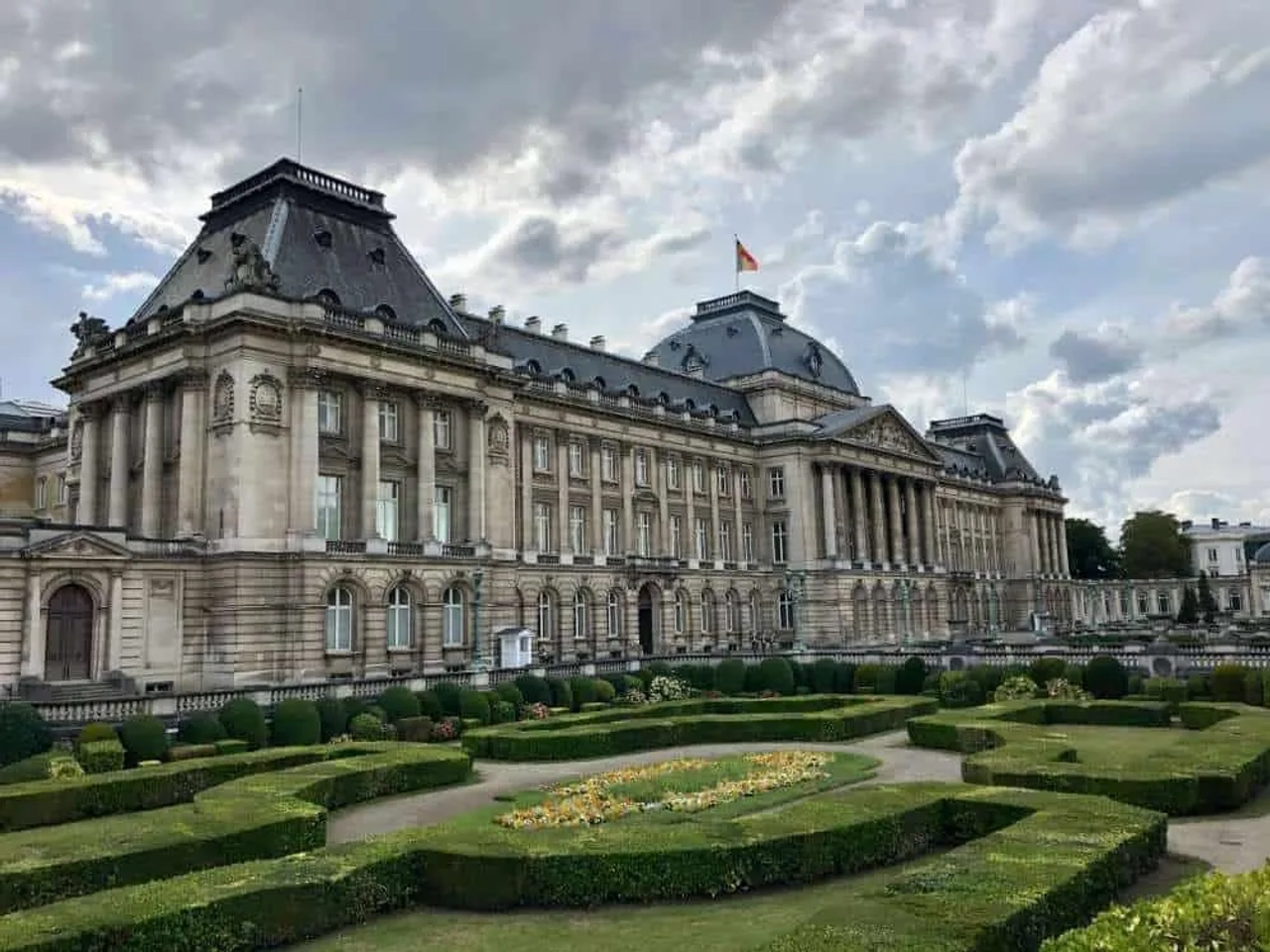 Palacio Real de Bruselas rodeado de jardines bien cuidados y nubes en el cielo.