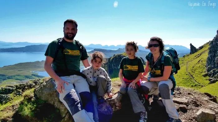 Familia sentada en una roca, disfrutando de un paisaje montañoso y soleado.