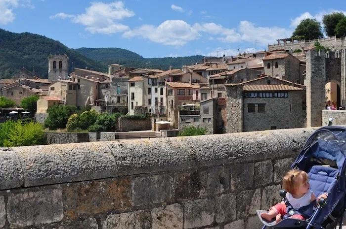 Vista de un pueblo con un bebé en un cochecito, rodeado de montañas.