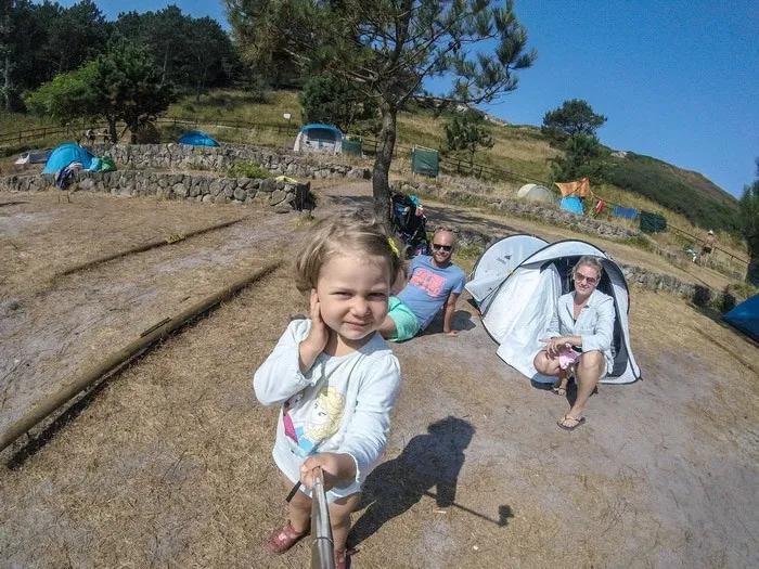 Niña sonriente con familia en un camping, rodeados de tiendas y naturaleza.