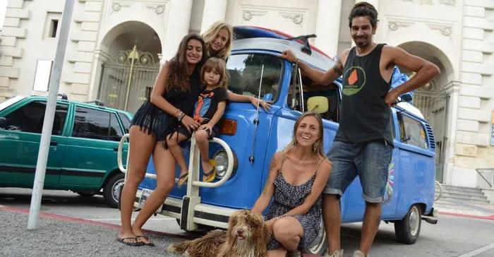 Familia sonriente posando frente a una furgoneta azul con un perro.