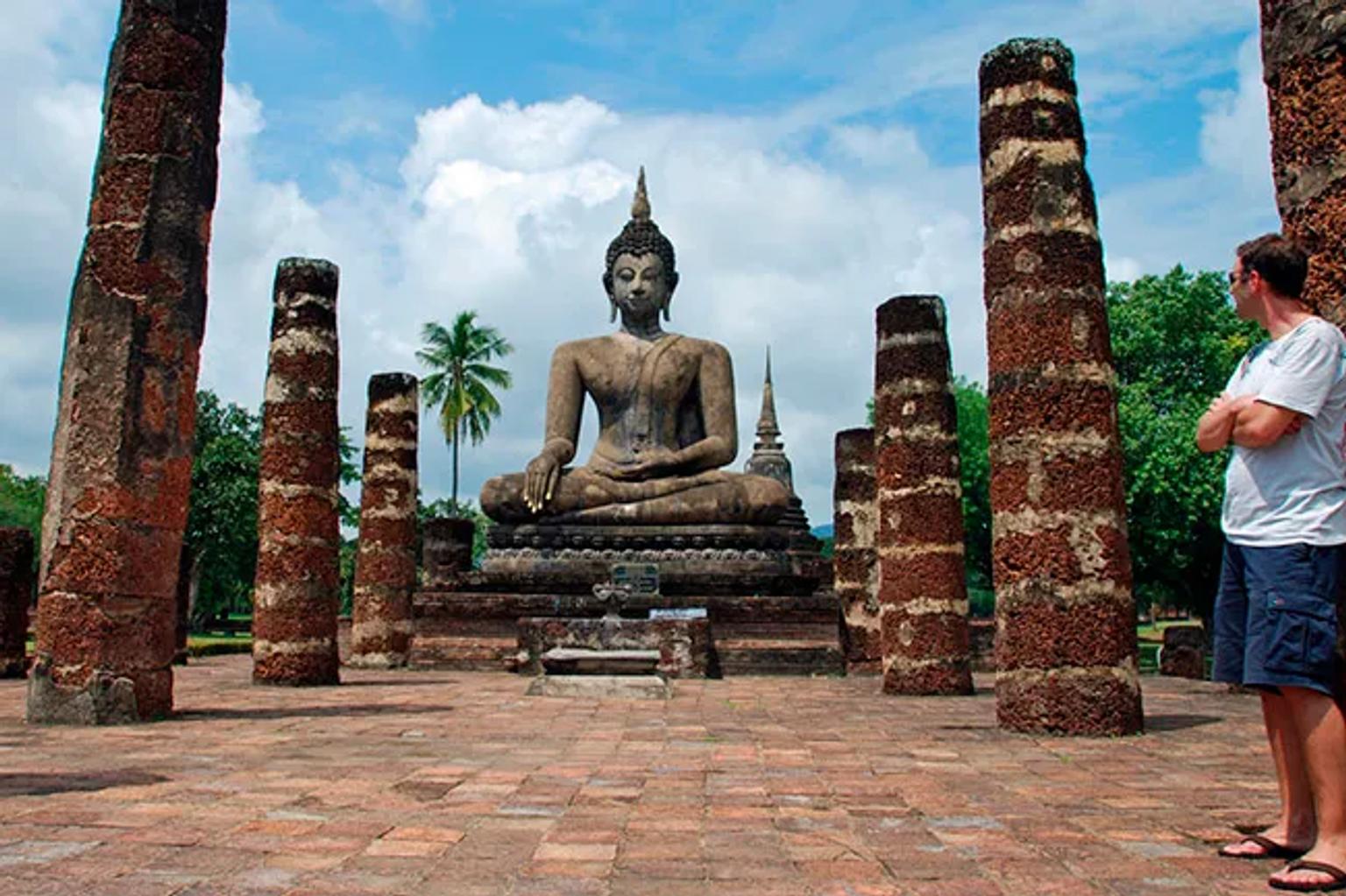 Buda monumental rodeado de columnas antiguas en un paisaje tropical.