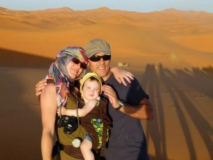 Familia sonriente en el desierto, con un niño pequeño y paisajes de arena.