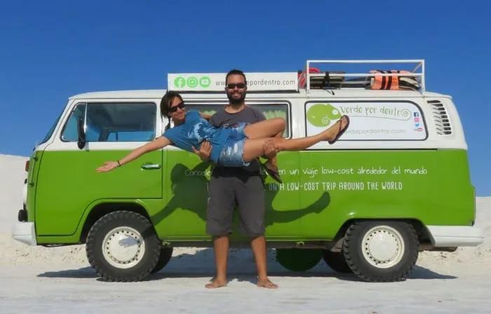 Pareja sonriente frente a una furgoneta verde en un paisaje desértico.