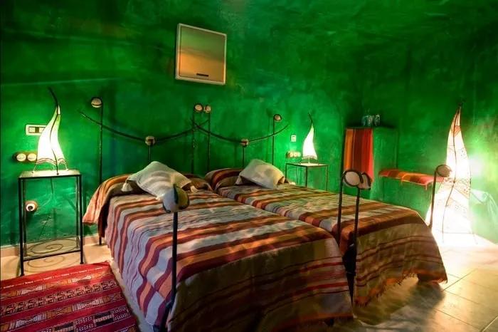 Habitación de hotel con paredes verdes, camas individuales y decoración original.