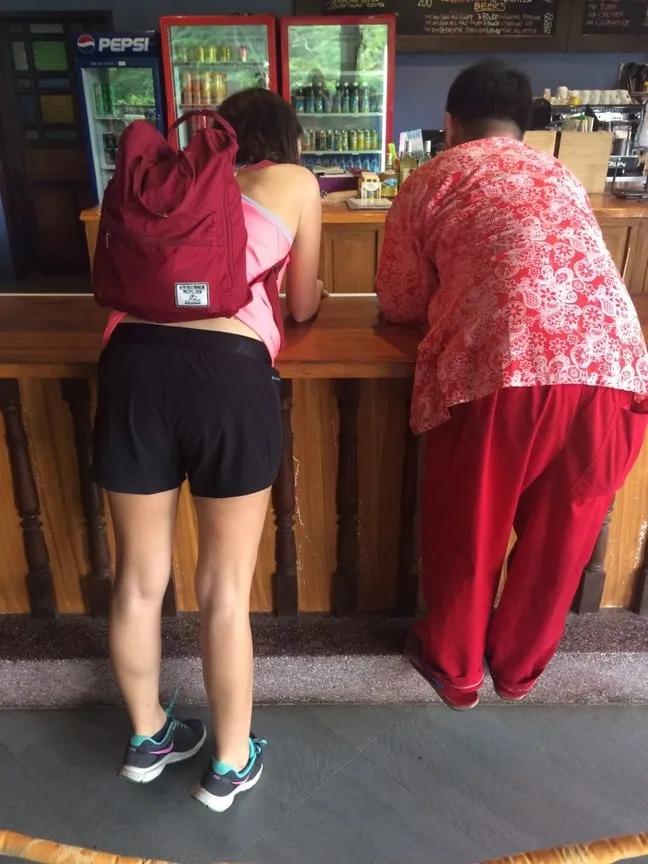 Dos personas de espaldas en un mostrador, una con mochila y otra en ropa colorida.