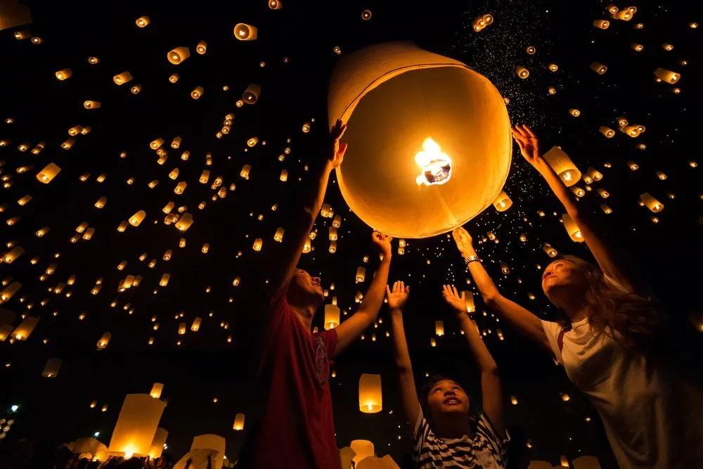 Familia lanzando linternas en un festival nocturno iluminado por luces flotantes.
