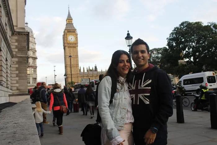 Pareja sonriente frente al Big Ben en Londres, rodeada de turistas.