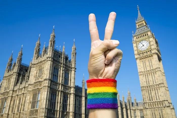 Mano con pulsera arcoíris haciendo signo de paz frente al Big Ben.