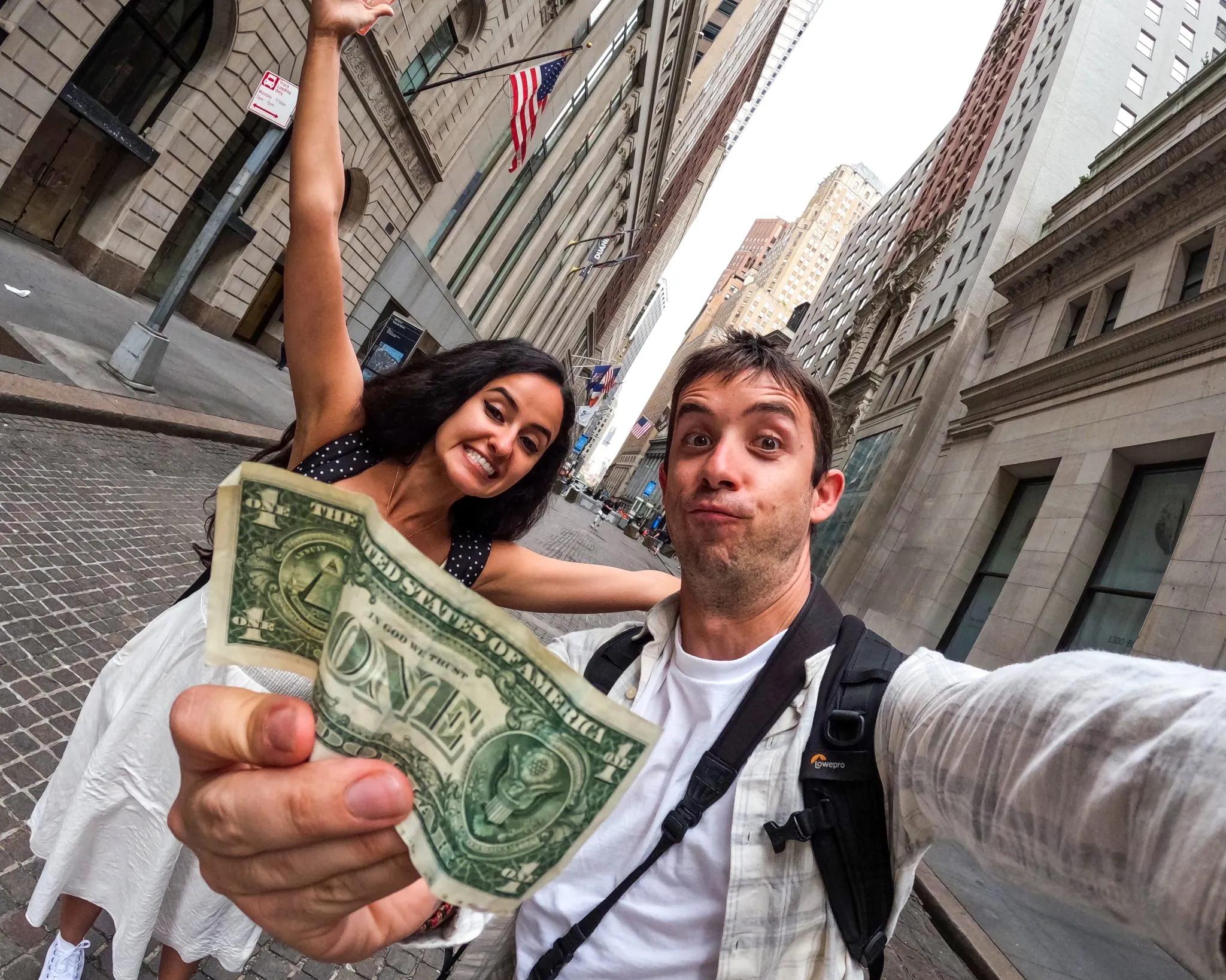 Pareja sonriente en la calle, mostrando un billete de un dólar.