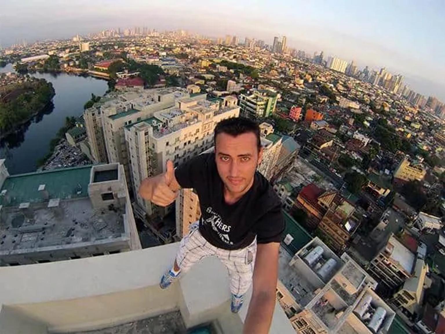Hombre haciendo un gesto de aprobación en un edificio alto con vista panorámica de la ciudad.