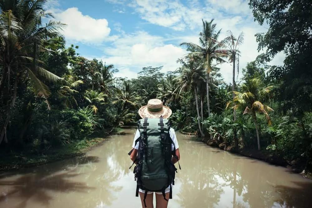 Persona con mochila frente a un río rodeado de vegetación tropical.
