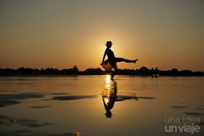 Silueta de mujer bailando al atardecer, reflejada en el agua.