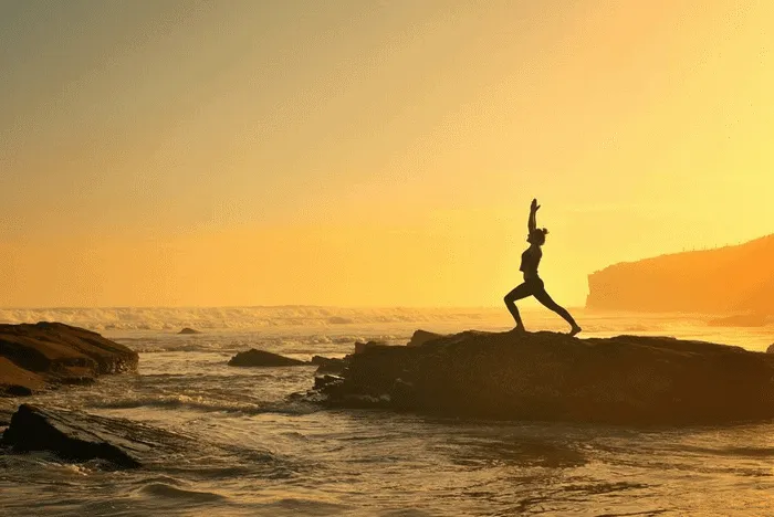 Silueta de una persona haciendo yoga en una roca frente al mar al atardecer.