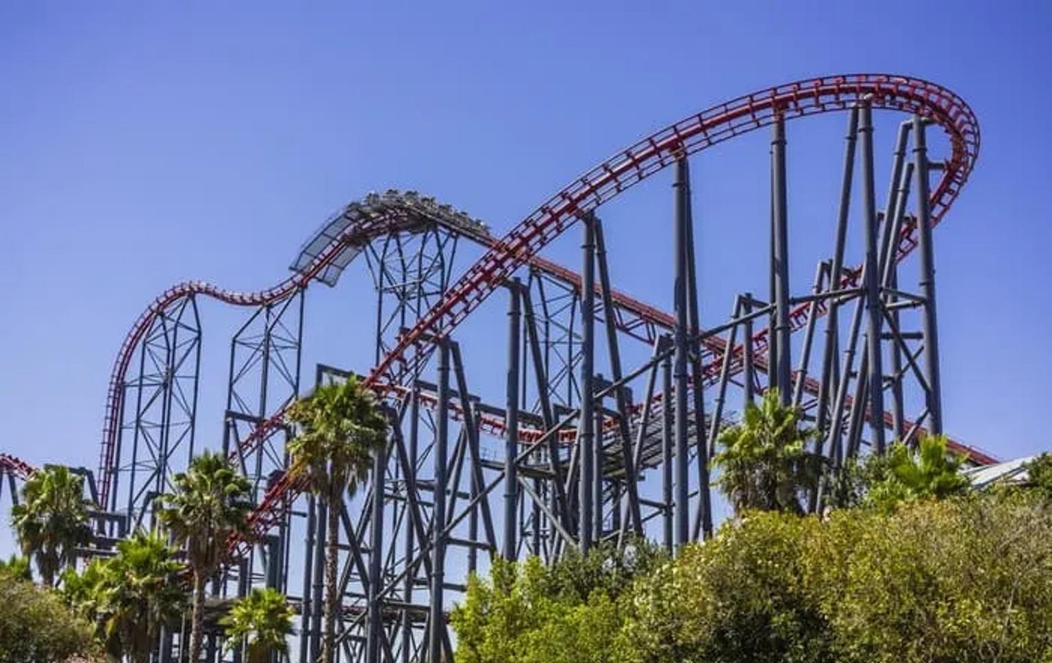 Montaña rusa en un parque temático, rodeada de palmeras y cielo azul.