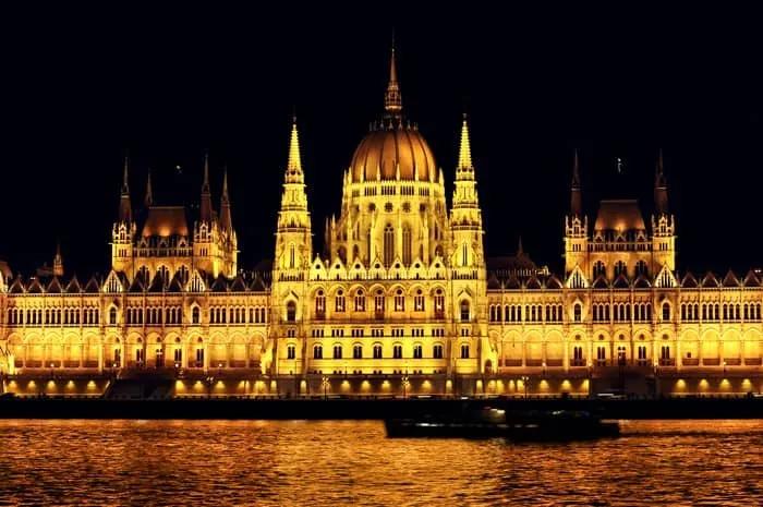 Edificio del Parlamento de Budapest iluminado por la noche, reflejándose en el agua.