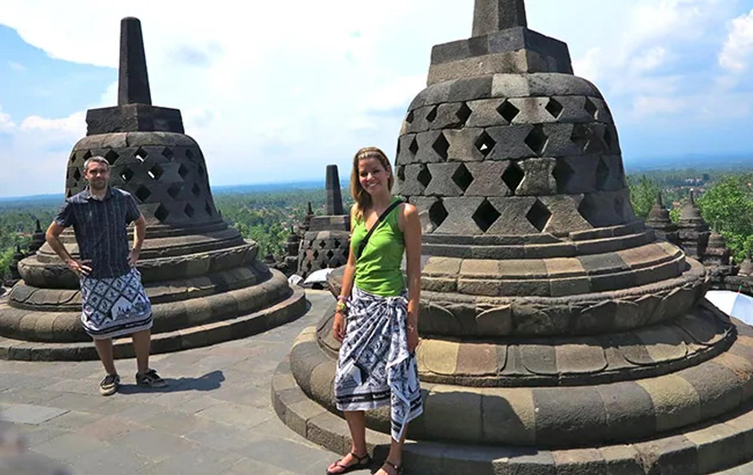 Pareja de viajeros en el templo de Borobudur, rodeados de estupas y paisaje verde.