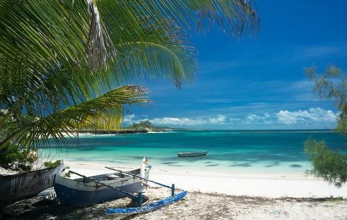 Playa tropical en Madagascar con palmeras y botes de pesca. Agua cristalina.