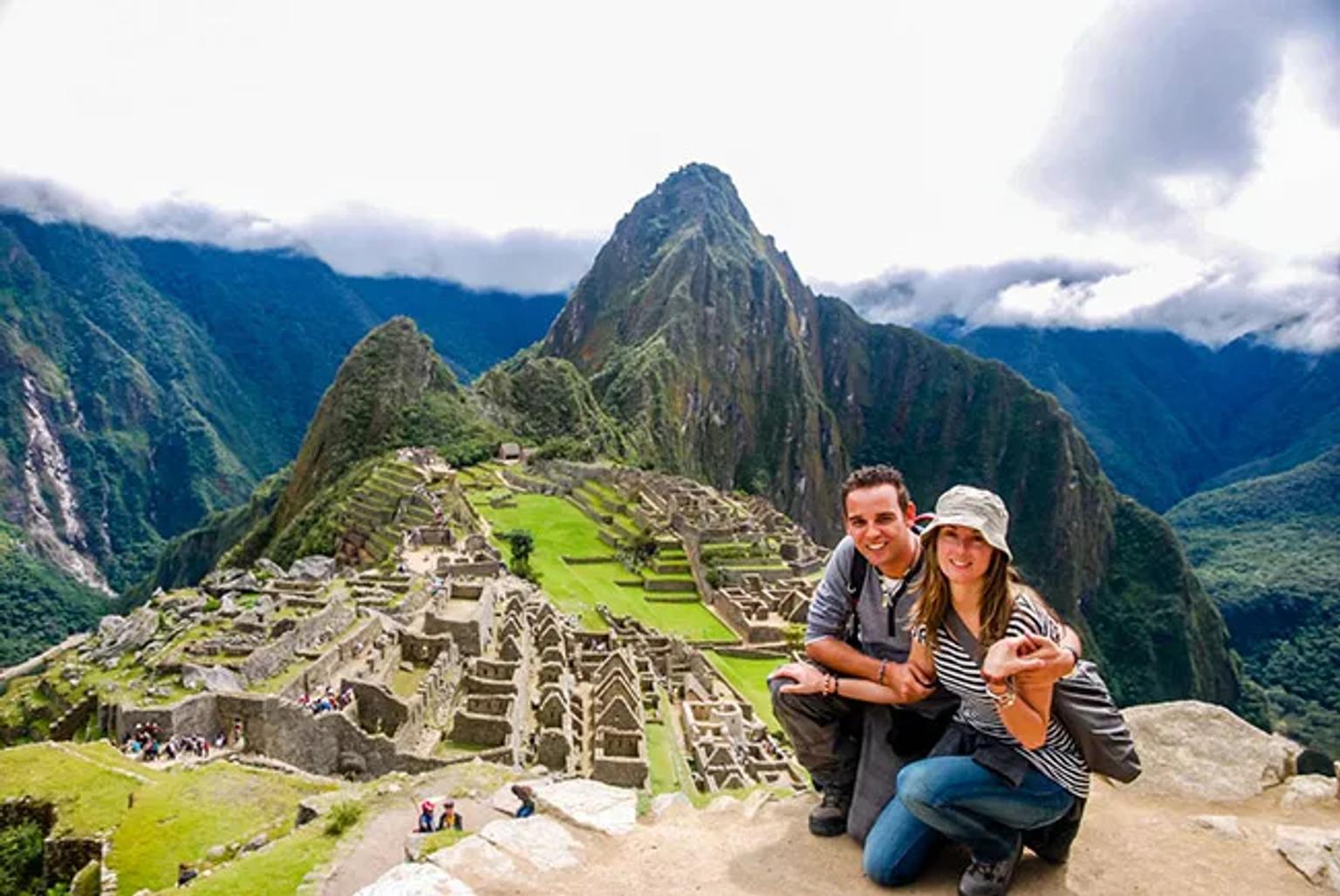 Pareja sonriente en Machu Picchu, con montañas y ruinas incas de fondo.