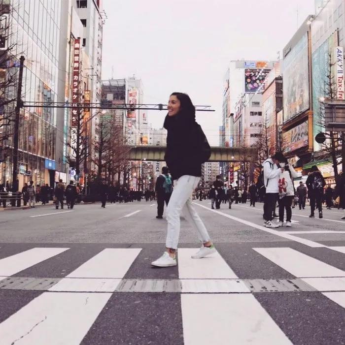 Mujer sonriente cruzando una calle concurrida en una ciudad moderna.