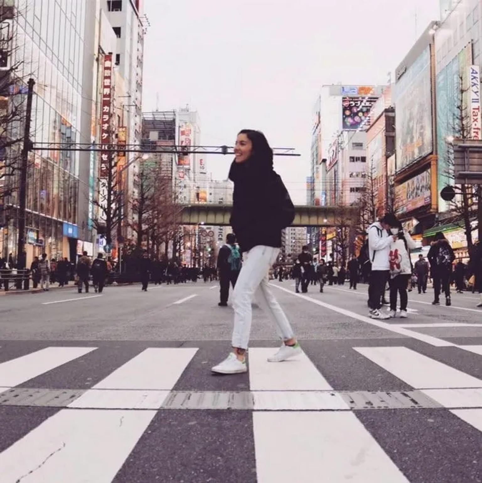 Mujer sonriente cruzando una calle concurrida en una ciudad moderna.