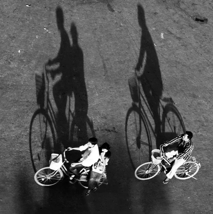Dos personas montando bicicletas, proyectando sombras alargadas sobre el suelo.