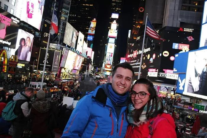 Pareja sonriente en Times Square, rodeada de luces y multitudes.