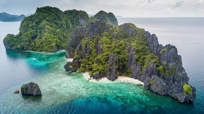 Isla tropical con formaciones rocosas, vegetación exuberante y aguas cristalinas.