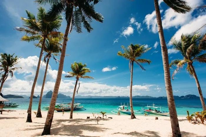 Playa tropical con palmeras y botes en aguas cristalinas de Filipinas.