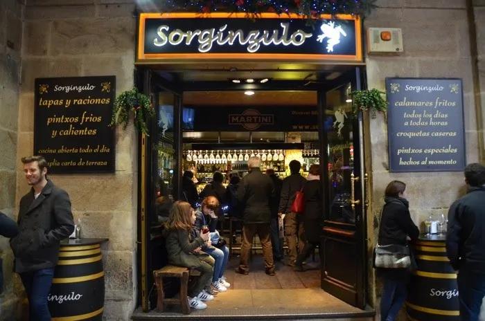 Entrada del bar Sorgingulo, con gente disfrutando pintxos y tapas en Bilbao.