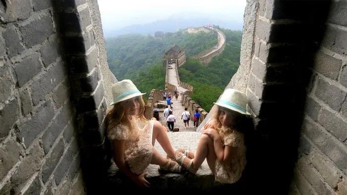 Dos niñas sentadas en la Gran Muralla China, rodeadas de turistas y naturaleza.