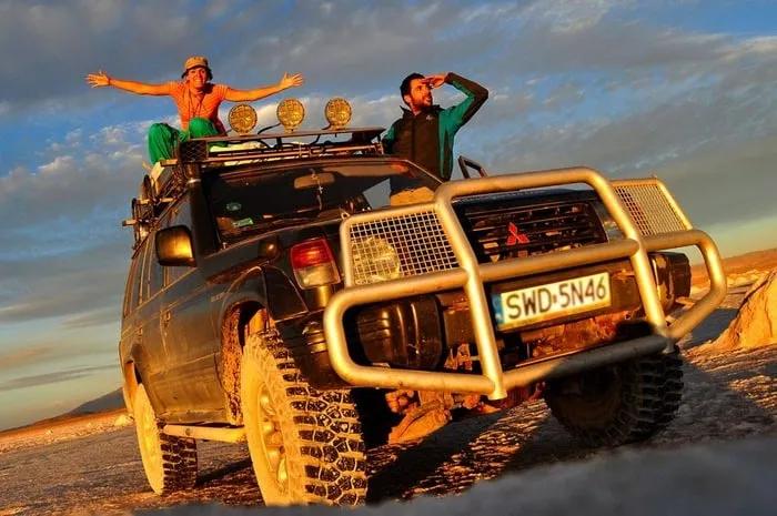 Dos personas sobre un vehículo todoterreno en un paisaje desértico al atardecer.