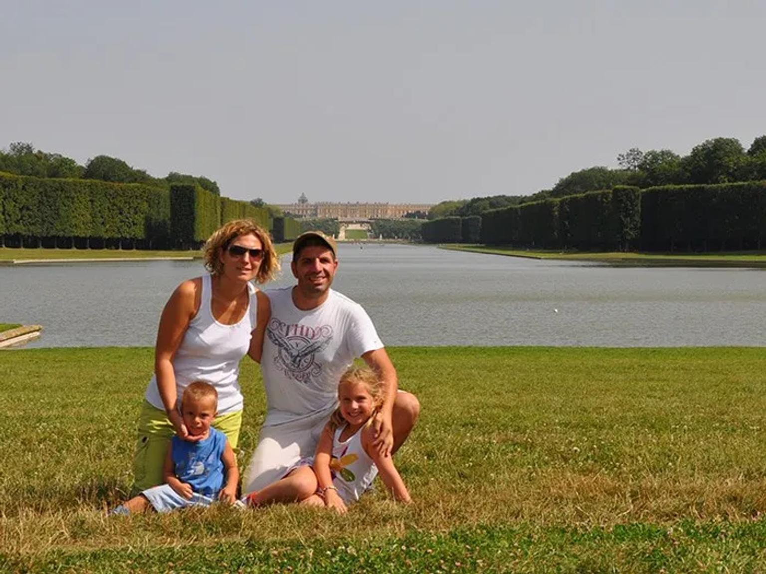 Familia posando frente a un lago y jardines en un día soleado.