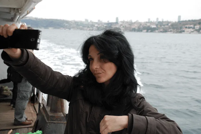 Mujer tomando una selfie en un barco con paisaje urbano al fondo.