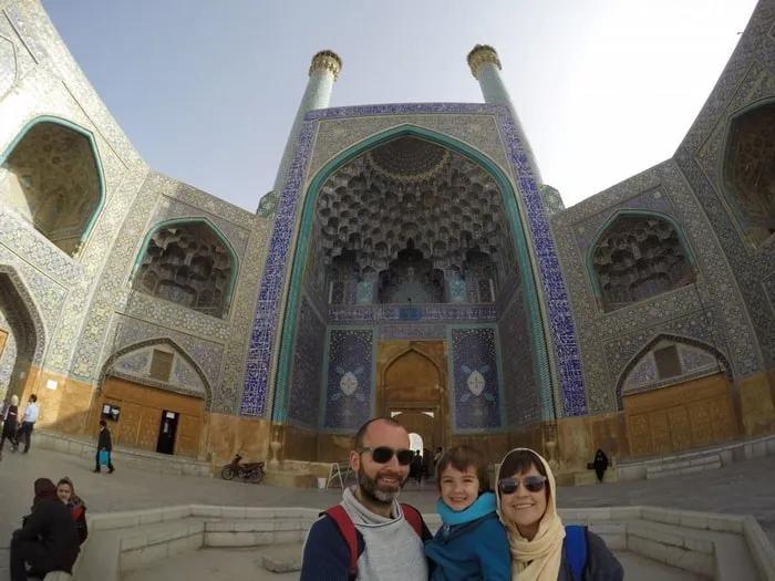 Familia sonriente frente a un majestuoso edificio con azulejos decorativos.