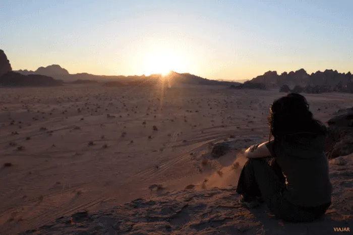 Mujer contemplando un amanecer en un desierto montañoso.