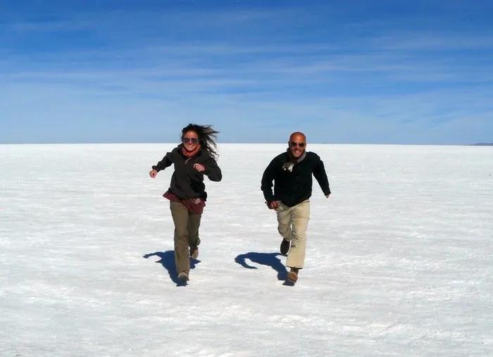 Dos personas corriendo sobre un paisaje de sal bajo un cielo azul.