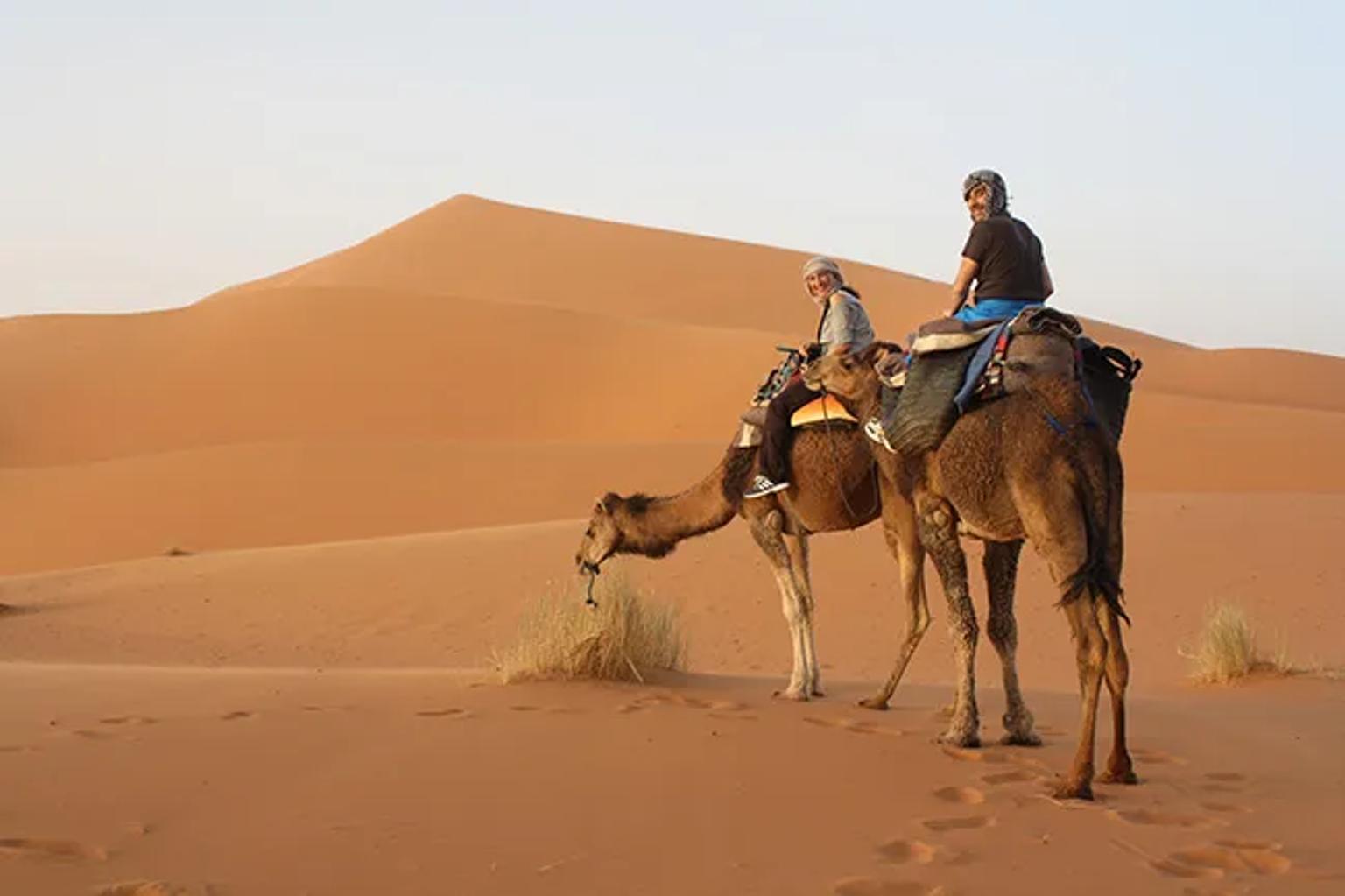 Pareja montando camellos en un desierto con dunas de arena.