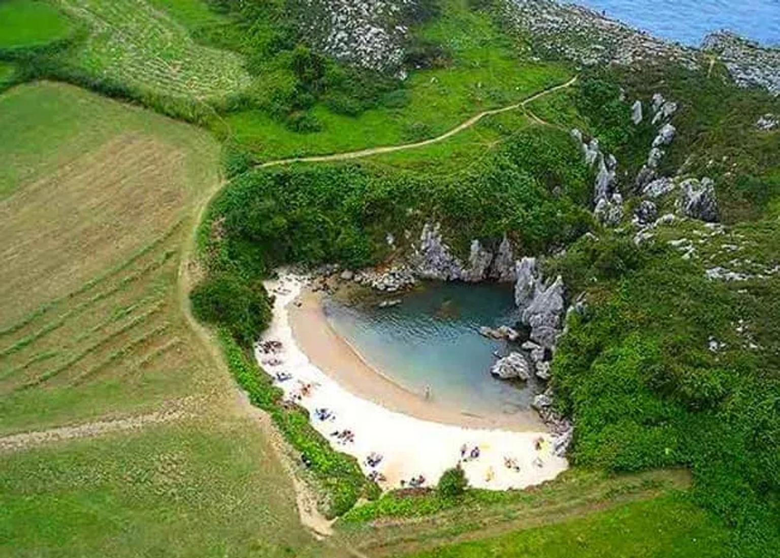 Playa escondida rodeada de vegetación y acantilados, con arena y agua cristalina.