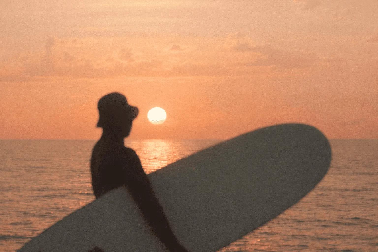 Silueta de un surfista al atardecer frente al mar.