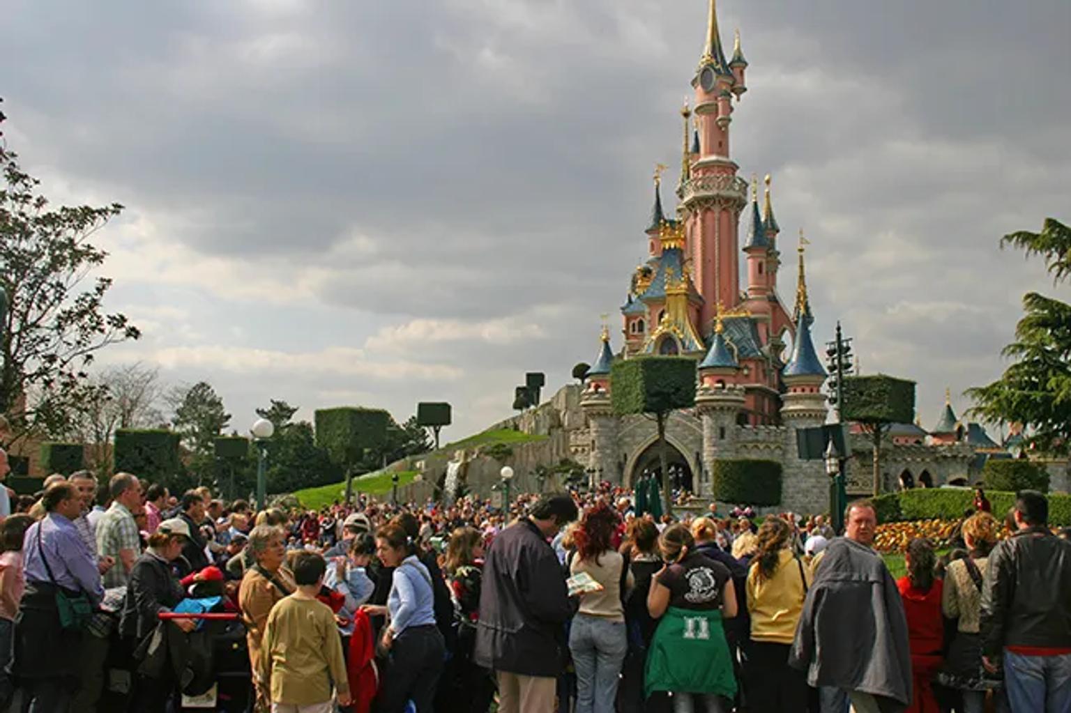 Multitud de visitantes frente al castillo en un parque de atracciones de Disney.