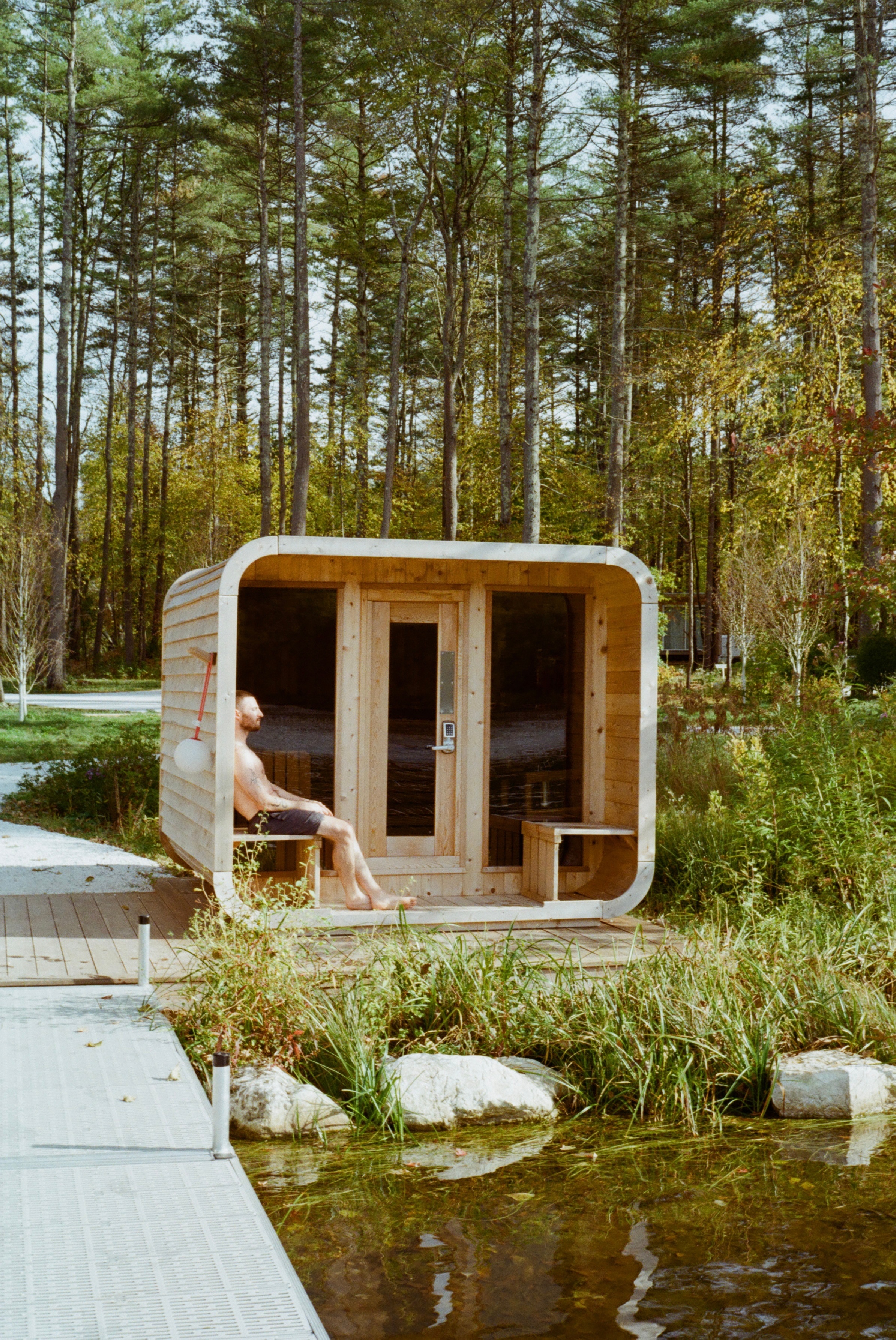 a cabin surrounded by tall trees with a man sitting in the opening space