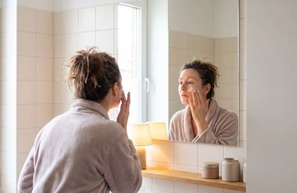 Una donna sui quarant’anni davanti allo specchio del bagno, ripresa da dietro.